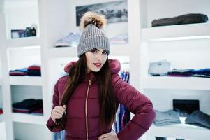 hermosa chica morena en la boutique de la tienda de ropa en chaqueta de invierno roja con sombrero. foto