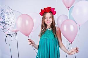 chica feliz con vestido verde turquesa y corona con globos de colores aislados en blanco. celebrando el tema del cumpleaños. foto