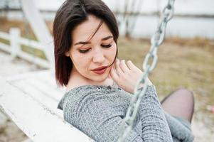 Portrait of brunette girl in gray dress sitting at white wooden construction. photo