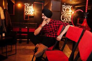 Indian man in checkered shirt and black turban sitting at bar. photo