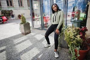 City portrait of positive young dark skinned female wearing green hoody. photo