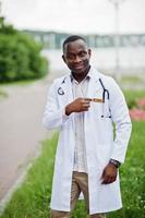 Young african american male doctor in white coat with a stethoscope posed outdoor. photo