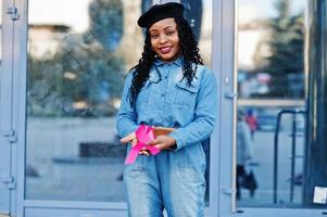 The power to fight. Stylish fashionable african american women in jeans wear and black beret against modern building with pink ribbon for breast cancer.