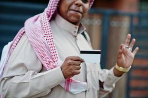 Middle Eastern arab business man posed on street against modern building with black handbag and credit card at hand. photo