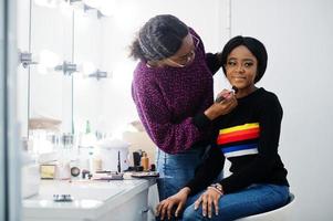 African American woman applying make-up by make-up artist at beauty saloon. photo