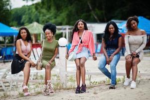 Group of five african american girls relaxing at beautiful poolside cabana beside luxury resort. photo