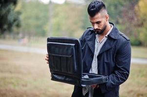 Fashionable tall arab beard man wear on black coat with bag case posed at rain weather day. photo
