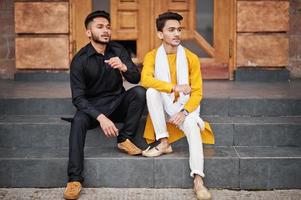 Two indian stylish mans friends in traditional clothes posed outdoor and sitting on stairs. photo