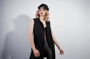 Studio portrait of blonde girl in black wear and cap against white background. photo