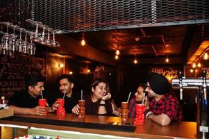 Group of indian friends having fun and rest at night club, drinking cocktails near bar counter. photo