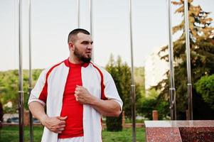 joven musculoso barbudo brutal vestido con traje deportivo blanco con camisa roja. foto