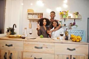 Three african american friends spending time at kitchen with wine. Black peoples relaxing at home. photo