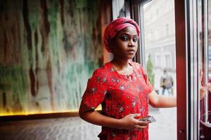 Stylish african woman in red shirt and hat posed indoor cafe. photo