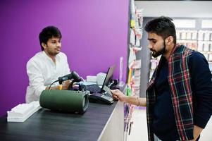 Indian man customer buyer pay for his new smartphone for seller by credit card at mobile phone store. South asian peoples and technologies concept. Cellphone shop. photo