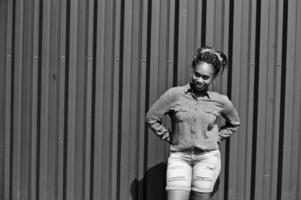 African woman with dreads hair, in jeans shorts posed against green steel wall. photo