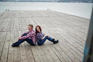 Stylish couple wear on checkered shirt in love together sitting on pier. photo