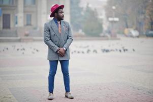 Stylish African American man model in gray jacket tie and red hat posed on street with fog. photo