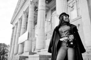 African american fashion girl in coat and newsboy cap posed at street. photo