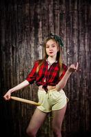 Young funny housewife in checkered shirt and yellow shorts pin up style with kitchen rolling pin on wooden background. photo