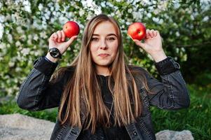 joven morena en jeans sentada en cuadros contra el árbol de flores de primavera y muestra ojos de manzana. foto