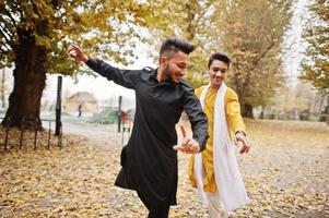 Two indian stylish mans friends in traditional clothes dancing outdoor. Navaratri dance. photo