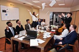 Multiracial business team meeting around boardroom table, two team leaders throw paper up. photo