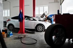 tema de reparación y mantenimiento de automóviles. mecánico en uniforme que trabaja en el servicio de automóviles, revisando el motor. foto