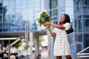 Beautiful african american girl holding bouquet of white roses flowers on dating in the city. Black businesswoman with bunch of flowers. photo