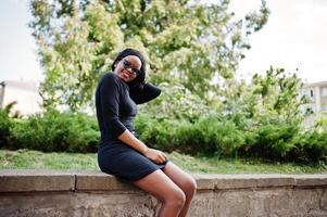 African american girl in sunglasses, black clothes and shirt sitting outdoor. Fashionable black woman. photo
