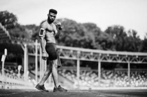 atleta masculino afroamericano sexy deporte torso desnudo hombre con funda de brazo deportivo para teléfono móvil, posó en el estadio. foto