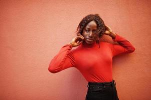 retrato de una mujer africana de pelo rizado con cuello alto rojo de moda posando contra una pared de rosas. foto