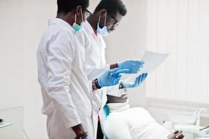 African american man patient in dental chair. Dentist office and doctor practice concept. Professional dentist helping his patient at dentistry medical. Pointing at teeth X-ray. photo