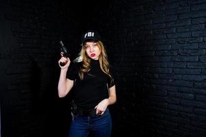 FBI female agent in cap and with gun at studio against dark brick wall. photo