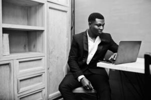 Strong powerful african american man in black suit sitting and working with laptop. photo