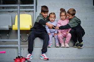 cuatro lindos niños sentados en el área deportiva y mirando el teléfono móvil. foto