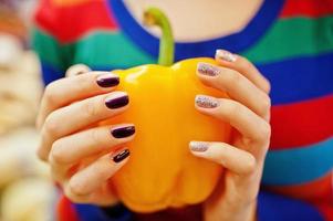 manos con manicura de ropa de niña en suéter de color, agujereando pimiento rojo. foto