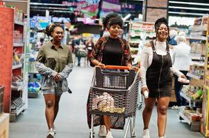 Three african american womans with shopping cart walking at supermarket. photo