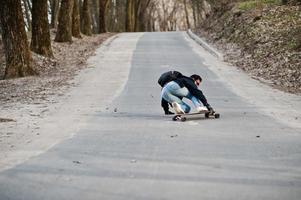 fallar al caer de una patineta. hombre árabe de estilo callejero en anteojos con longboard longboarding por el camino. foto