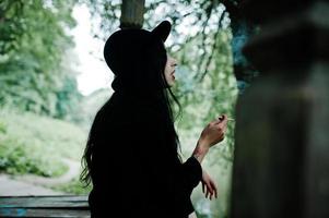 Sensual smoker girl all in black, red lips and hat. Goth dramatic woman smoking thin cigarette. photo