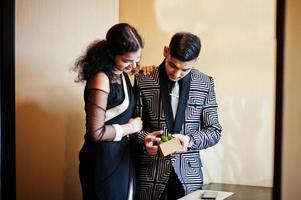 Lovely indian couple in love, wear at saree and elegant suit, posed on restaurant and hold green plant. photo