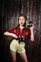 Young funny housewife in checkered shirt and yellow shorts pin up style with saucepan on wooden background. photo