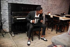 Strong powerful african american man in black suit sitting against piano. photo