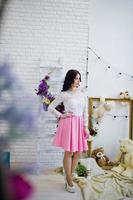 Young brunette girl in pink skirt and white blouse posed indoor against room with toys bear. photo