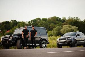 dos hermanos asiáticos se visten de negro y posan cerca de los autos todoterreno. foto