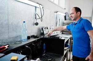 Car repair and maintenance theme. Electric mechanic in uniform working in auto service, making car diagnostics using obd device with laptop. photo