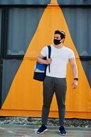 Portrait sports arabian man in black medical face mask with backpack posed against yellow triangle during coronavirus quarantine. photo