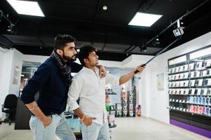 dos indios sirven al comprador del cliente en el teléfono móvil haciendo selfie con un palo monopie. concepto de pueblos y tecnologías del sur de Asia. tienda de celulares foto