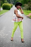 Amazing african american model woman in green pants and black hat posed with different emotions at park. photo