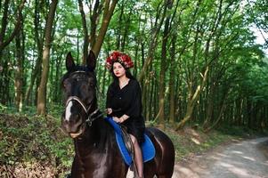 chica mística en ropa de corona en negro a caballo en madera. foto