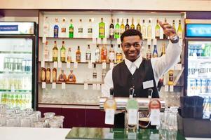 camarero afroamericano en el bar que vierte cerveza fresca en el vaso en el pub. foto